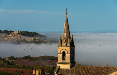 view of church tower at Bonnieux hiitop village in  provence  France with Lacoste in the background misty autumn morning seen from the luberon mountain . - Powered by Adobe