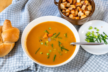Carrot soup in plate, bread, onion shoot and piece of fried bread in bowl.