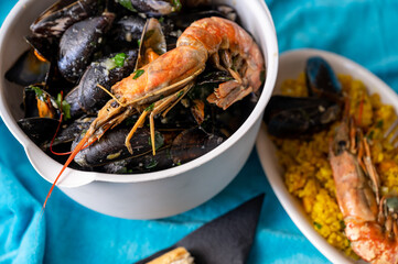 Big bowl with boiled black mussel and shrimp and small plate with paella.