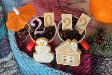 gingerbread snowman and house, cups with coffee beans and the number 2022 surrounded by knitted scarves top view. Happy New Year and Merry Christmas