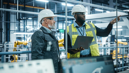 Car Factory: Project Manager and Automotive Engineer in Hard Hat, Talking, Using Laptop....