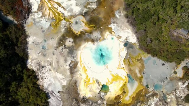 Impressive colorful geothermal area with emerald steaming hot spring, silica terrace, mud pools and geysers. Aerial top down rising at Orakei Koraku, Aotearoa