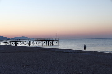 Beach pier and silhouette against the background of the calm sea and mountains at sunrise,...