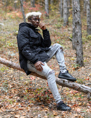 Autumn nature with human. Young african american man resting in the forest, sitting on a fallen tree