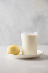 Vegan potato milk in glass and potato in bowl on white background. Vertical format. Close up. Plant based milk replacer and lactose free.