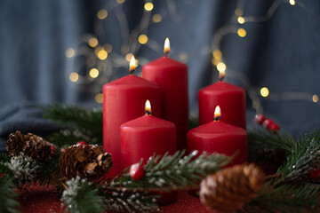 Christmas decoration with red candles, spruce branches, cones and garland on red table on blurry background. Side view. New year mood, festive concept, holiday table, gift card.