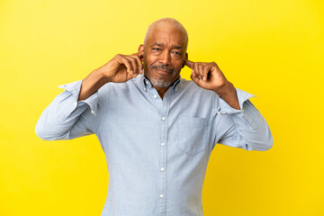 Cuban Senior isolated on yellow background frustrated and covering ears