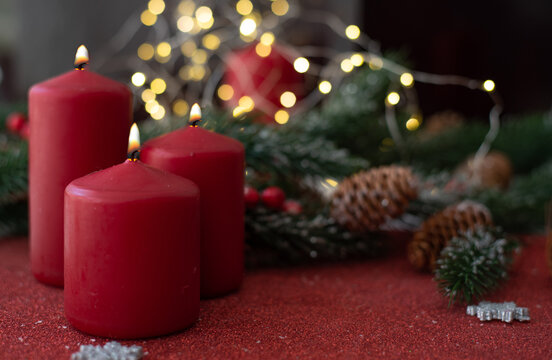 Christmas decoration with red candles, spruce branches and cones on red table on blurry background with yellow bokeh. Side view.  New year mood, festive concept, holiday table, gift card