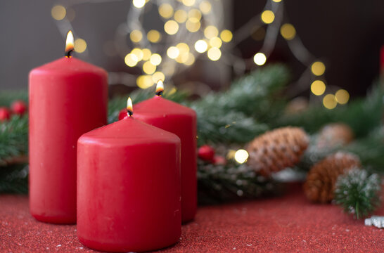 Christmas decoration with red candles, spruce branches and cones on red table on blurry background with yellow bokeh. Side view.  New year mood, festive concept, holiday table, gift card