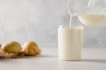 Pouring vegan potato milk in glass and potato in bowl on light background. Close up. Plant based...