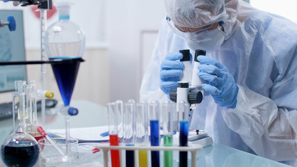Fototapeta premium Closeup of scientist chemist doctor wearing ppe equipment analyzing sample with virus using medical microscope during microbiology experiment in hospital laboratory. Medicine concept