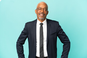 Business senior man isolated on blue background posing with arms at hip and smiling