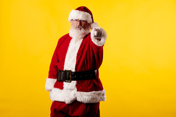 Fototapeta na wymiar Santa Claus pointing his finger at the camera on yellow background