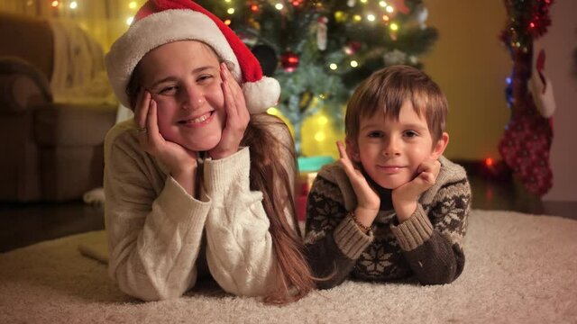 Smiling boy with mother lying on carpet under Christmas tree while celebrating New Year. Families and children celebrating winter holidays.