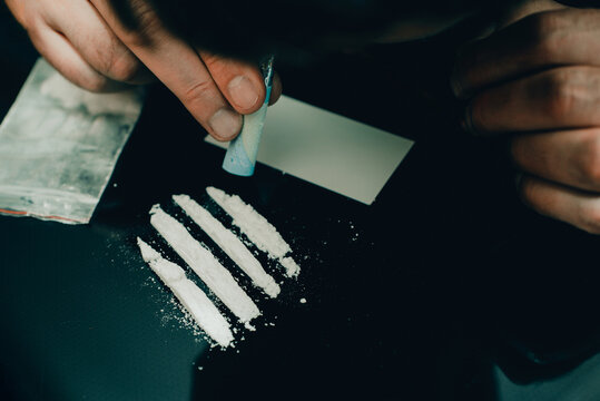 Drug addict. Drug abuse, man taking drugs, snorting lines of cocaine white powder, closeup, toned.