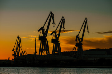 Fototapeta premium Shipyard crane silhouettes against orange dusk sky