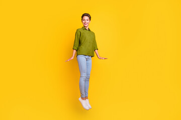 Fototapeta na wymiar Photo of carefree cheerful lady jump shy pose wear green shirt jeans sneakers isolated yellow color background