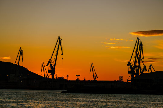 Harbour shipyard cranes against orange sky in Ferrol, Galicia, Spain