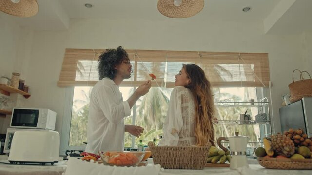 Young happy active married couple dancing laughing together cooking meals at home, carefree joyful husband and wife have fun cooking healthy breakfast food in boho styled kitchen