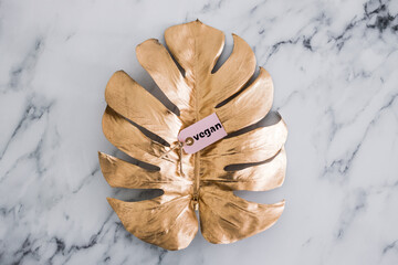 vegan label on top of golden leaf decoration on marble table, healthy nutrition and ethical choices