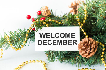 Welcome, December text on the card, which lies on a branch with New Year's decor.