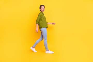 Photo of cheerful positive carefree lady walk wear green shirt jeans shoes isolated yellow color background