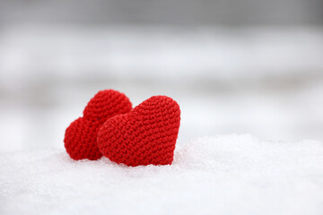 Fototapeta premium Love hearts in the snow in a park. Valentine's card, two red knitted symbols of love, background for romantic event in winter, Christmas celebration
