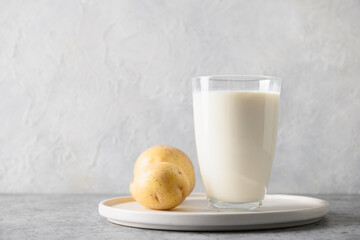 Vegan potato milk in glass and potato in bowl on gray background. Close up. Plant based milk replacer and lactose free.