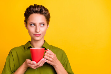 Photo of cunning minded lady hold cup look empty space wear green shirt isolated yellow color...