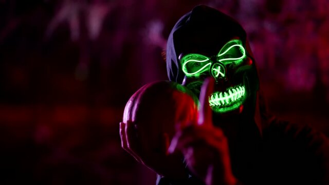 dangerous mystical ghost with glowing skull is holding pumpkin and wagging finger to camera