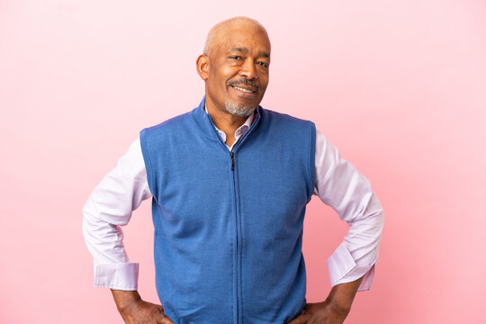 Cuban senior isolated on pink background posing with arms at hip and smiling