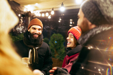 Close-up happy smiling friends with cups of mulled wine spending time together at winter fair at evening. Holidays, Christmas concept