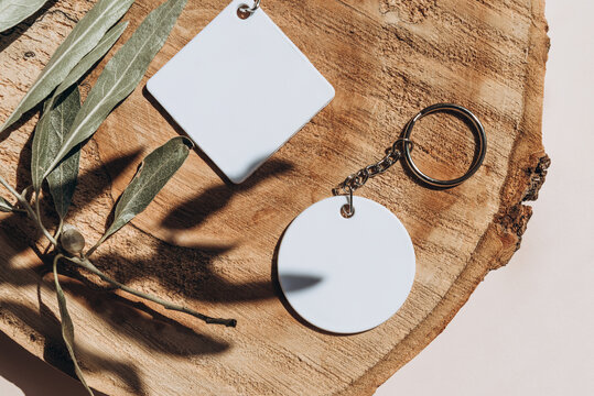 Keychain mockup among olive leaves to display design. Blank white sublimation key chain photo.