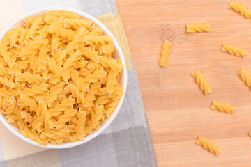 Uncooked Fusilli Pasta in White Bowl on Wooden Board. Raw and Dry Macaroni. Unhealthy and Fat Food. Italian Culture