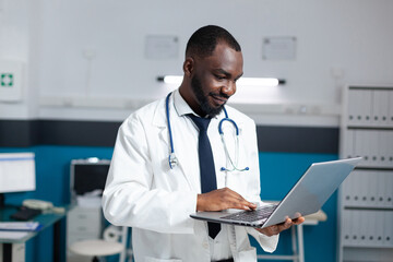 African american therapist doctor holding laptop computer looking at online medicine prescription...