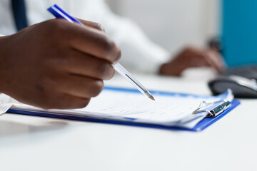 Closeup of african american therapist doctor analyzing medicine prescription paperwork monitoring sickness patient expertise. Practitioner man working at healthcare treatment in hospital office