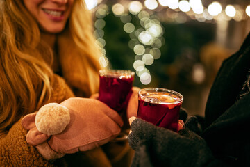 Close-up woman's hands in winter mittens with hot cup of hot mulled wine. Holidays, traditions,...