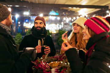 Happy smiling friends with cups of mulled wine having fun, spending time together at winter fair at evening. Holidays, Christmas concept