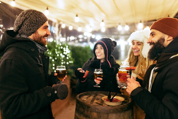 Happy smiling friends with beer glasses having fun, spending time together at winter fair at evening. Holidays, Christmas concept