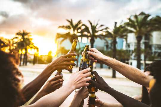 Group Of Multiethnic Happy Friends Having Party Outside Celebrating Toasting Beer Bottles On Sunset - Young People Hanging Out Drinking Alcohol Together - Celebration And Happiness Concept