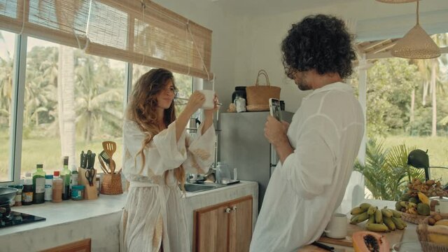Young happy active married couple dancing laughing together cooking meals at home, carefree joyful husband and wife have fun cooking healthy breakfast food in boho styled kitchen