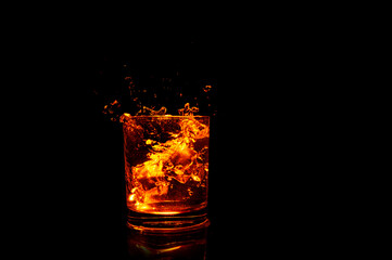 glass with brown liquid with ice cubes and bottom illumination on dark background