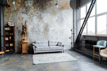 interior shot in the loft studio.Large panoramic window,a lot of light, an unusual decorative wall, A bookcase full of books. a chic gray sofa. Arrangement of furniture.