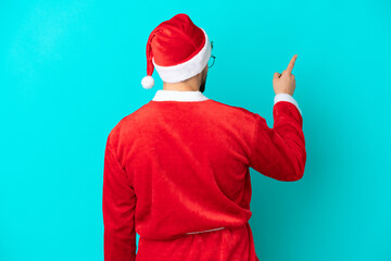 Fototapeta na wymiar Young man disguised as Santa Claus isolated on blue background pointing back with the index finger