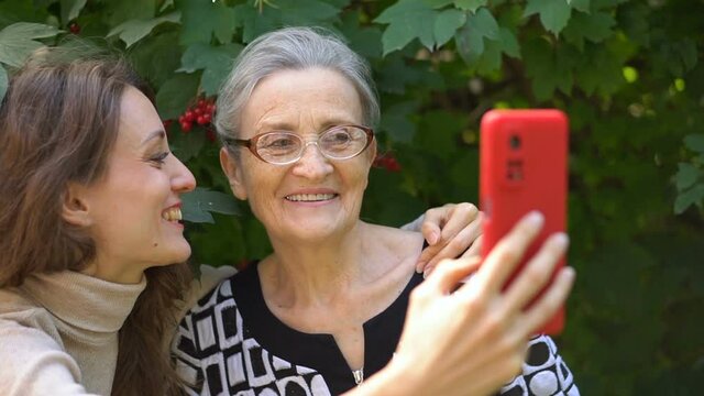 Adult daughter and senior mum are taking self-portrait picture, selfie on red smartphone together, happy retirement, mothers day concepts.