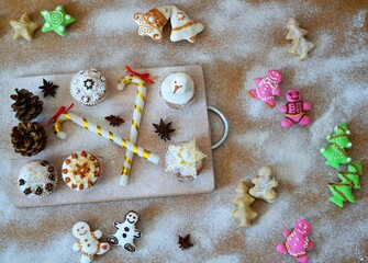 Christmas composition: cookies in the shape of a Christmas tree, gingerbread man, bells and colorful stars decorated on a background of powdered sugar and wood