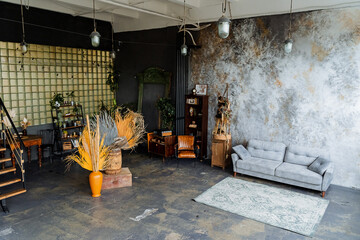 interior shot in loft studio.a lot of light, an unusual decorative wall, A bookcase full of books. a chic gray sofa, a vase with dry leaves, nearby stairs