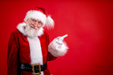 Santa Claus pointing aside empty copy space on finger and looking showing blank place for advertised product or text on red studio background. Sale, Discount, Black Friday. Look at this