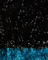 Christmas decorations view of blue shiny bright garland on dark background with silver colors bokeh on the bottom. Holidays concept with copy space