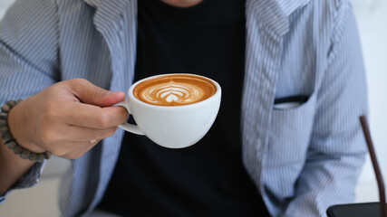 Closeup image of a young smart man holding a coffee cup with latte art in the comfortable living room.